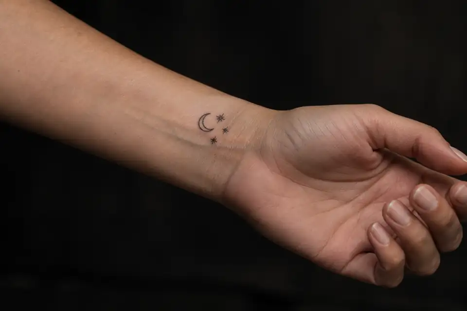 Small fine-line crescent and stars tattoo on an adult inner wrist